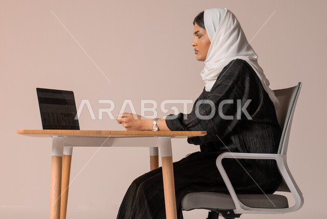 إدارة شؤون الأعمال وتنظيمه, احتراف وظائف الحاسب والتكنولوجيا، بورتريه لإمراه عربيه سعوديه خليجيه محجبة ترتدي عباءة سوداء  تجلس على كرسي مريح تنظر الى جهاز الحاسوب بايماءات الانزعاج، إنجاز المهام المكتبية، خلفية بيج