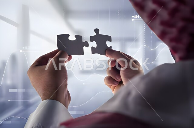 التركيز وحل اللغز، صورة مقربة ليد رجل سعودي خليجي يحمل قطعتين من اللغز يحاول ربط وتوصيل قطع  الصغيرة، مفهوم لعبة بازل ،  خلفية الاحصائيات الخاصة بالاسهم والبورصة بتقنية الهولوجرام، إيجاد حلول للألغاز وحل المشكلات