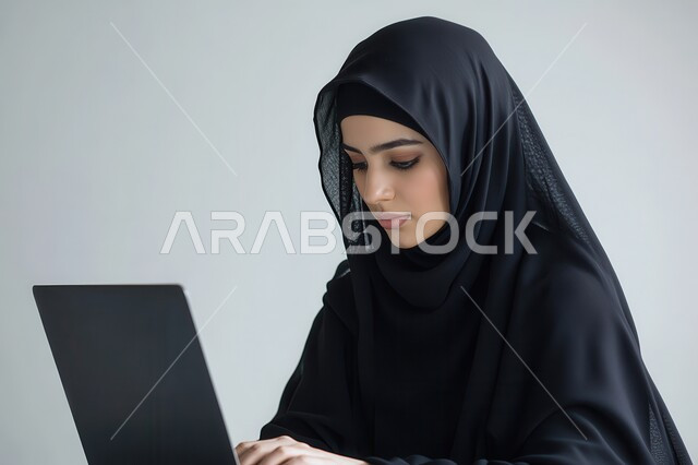 ايماءات التركيز والاندماج، دمج التكنولوجيا بالعمل، مهن ووظائف سعودية نسائية، ادارة الأعمال عن بعد، استخدام الأجهزة والتقنيات الحديثة والمتطورة، بورتريه مقرب لإمرأة عربية خليجية سعودية ترتدي العباءة والحجاب تقوم باستخدام الحاسب المحمول، خلفية بيضاء