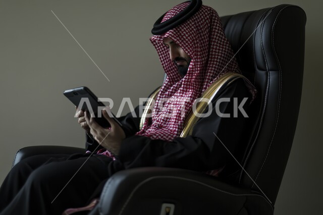 مهن ووظائف إدارية سعودية مكتبية، إجراء مقابلات عمل أونلاين, استخدام الأجهزة والتقنيات الحديثة لتسهيل الأعمال, رجل أعمال عربي سعودي خليجي يرتدي البشت الشماغ  يجلس على كرسي مريح ويستخدم جهاز التابلت, تحقيق استراتيجيات وأهداف العمل