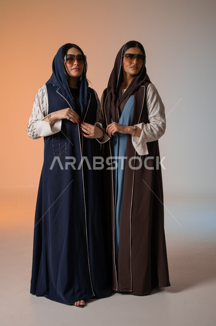 ارتداء العباءة الخليجية والنظارات الشمسية، ايماءات الثقة والوقوف أمام الكاميرا، الاحتراف في عرض آخر صيحات الموضة والجمال، بورتريه لعارضتان عربيتان سعوديتان خليجيتان، صورة الجسم بالطول الكامل، منتجات نسائيه سعوديه، شراء الأزياء والاكسسوارات, خلفية ملونة 