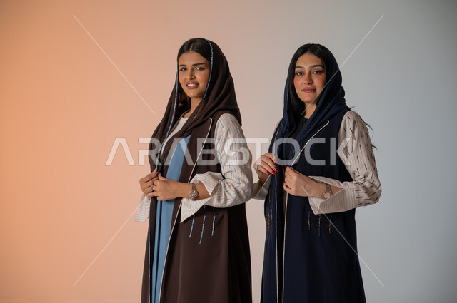 منتجات نسائيه سعوديه، ايماءات الثقة والوقوف أمام الكاميرا، ارتداء العباءة الخليجية والنظارات الشمسية، الاحتراف في عرض آخر صيحات الموضة والجمال، بورتريه لعارضتان عربيتان سعوديتان خليجيتان، شراء الأزياء والاكسسوارات, خلفية ملونة 
