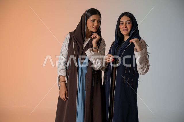 منتجات نسائيه سعوديه، ايماءات الثقة والوقوف أمام الكاميرا، ارتداء العباءة الخليجية والنظارات الشمسية، الاحتراف في عرض آخر صيحات الموضة والجمال، بورتريه لعارضتان عربيتان سعوديتان خليجيتان، شراء الأزياء والاكسسوارات, خلفية ملونة 