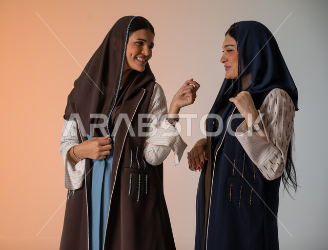 منتجات نسائيه سعوديه، ايماءات الثقة والوقوف أمام الكاميرا، ارتداء العباءة الخليجية والنظارات الشمسية، الاحتراف في عرض آخر صيحات الموضة والجمال، بورتريه لعارضتان عربيتان سعوديتان خليجيتان، شراء الأزياء والاكسسوارات, خلفية ملونة 