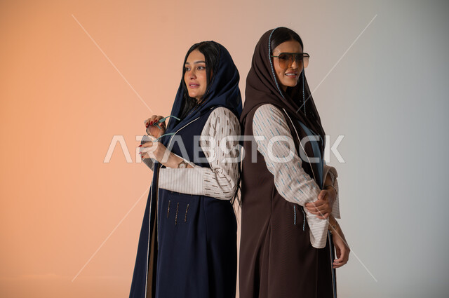 منتجات نسائيه سعوديه، ايماءات الثقة والوقوف أمام الكاميرا، ارتداء العباءة الخليجية والنظارات الشمسية، الاحتراف في عرض آخر صيحات الموضة والجمال، بورتريه لعارضتان عربيتان سعوديتان خليجيتان، شراء الأزياء والاكسسوارات, خلفية ملونة 