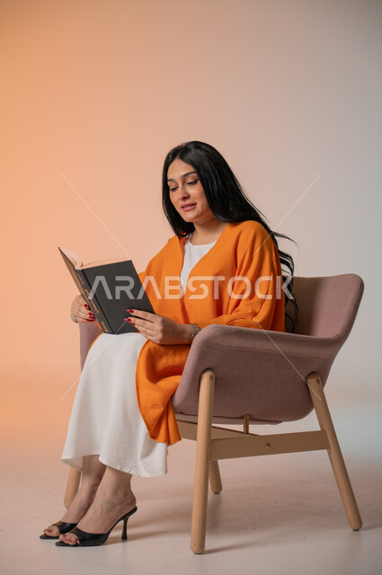 تنمية شغف المطالعة والثقافة، قراءة الكتب المتنوعة وتزويد الذخيرة الفكرية، بورتريه لامرأة أنيقة عربية خليجية سعودية ترتدي الزي الكاجوال تجلس على كرسي مريح وتحمل بيدها كتاب وتطالع فيه بإيماءات الاندماج والتركيز، أهمية تثقيف الأنثى لبناء مجمتع ناجح، خلفية ملونة