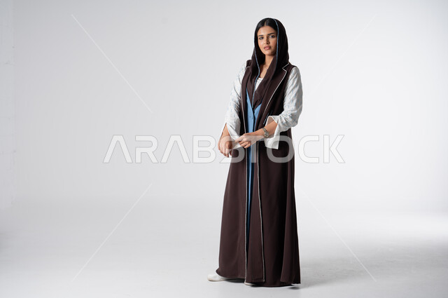 Women's abayas with distinctive modern designs, portrait of a Saudi Arabian Gulf woman wearing an elegant colorful abaya, concept of fashion and elegance, looking at the camera with gestures of self-confidence, interest in external appearance, full-length body image, white background