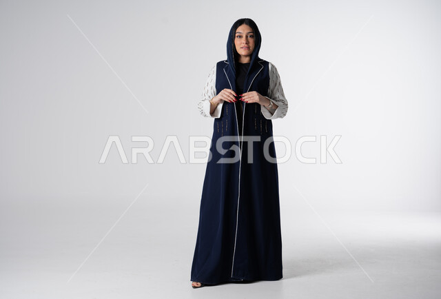 Women's abayas with distinctive modern designs, portrait of a Saudi Arabian Gulf woman wearing an elegant colorful abaya, concept of fashion and elegance, looking at the camera with gestures of self-confidence, interest in external appearance, full-length body image, white background