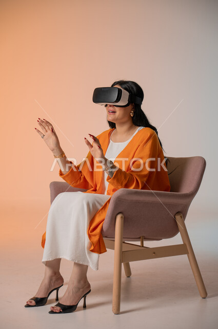 Gestures of interaction and integration with virtual reality, spending leisure time in an enjoyable way, a portrait of an elegant Saudi Arabian Gulf woman wearing a casual outfit sitting in a comfortable chair wearing VR glasses, using modern technical devices and technology to see imaginary scenes, a colorful background