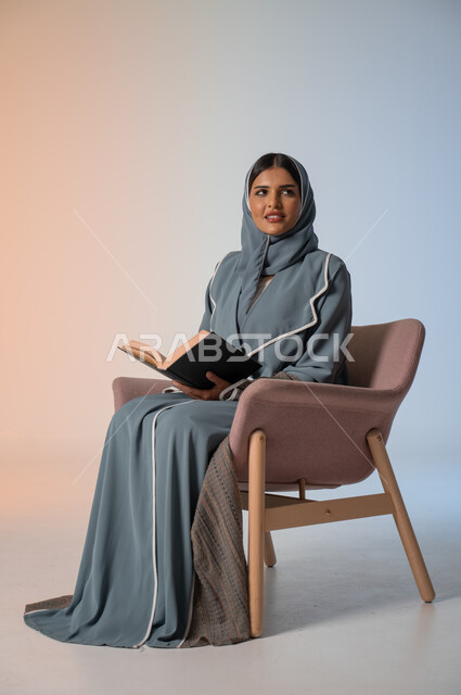  قضاء الوقت بالقراءة والتعلم والتثقف، بورتريه لامرأة عربية سعودية خليجية محجبة ترتدي العباءة تجلس على كرسي مريح وتحمل بيديها كتاب، الاستمتاع بقراءة الكتب والقصص والروايات, ثقافة التعلم الذاتي, خلفية ملونة