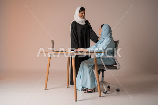 الشراكة والتعاون في إنجاز المهام، بورتريه لسيدتان عربيتان خليجيتات سعوديتان محجبتان في اجتماع عمل، استخدام جهاز الحاسوب المحمول لمتابعة ومناقشة الأعمال، دراسة وتحليل المشاريع الجديدة، اداء المهام للتطور المهني وتحقيق الاهداف, خلفية بيج