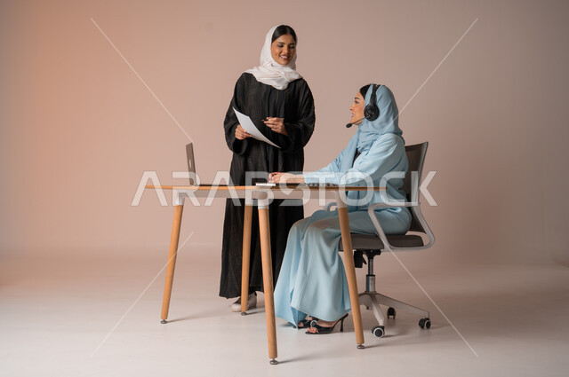 Study and analysis of new projects, performing tasks for professional development and achieving goals, partnership and cooperation in completing tasks, portrait of a veiled Saudi Gulf Arab employee wearing a black abaya, holding work papers in her hand, verifying the accuracy of information from the businesswoman, beige background