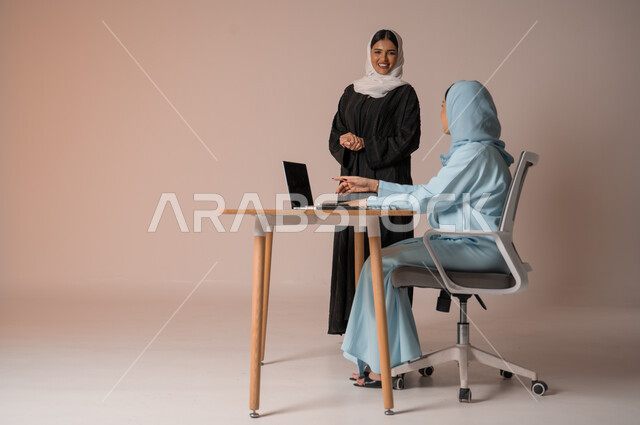 استخدام جهاز الحاسوب المحمول لمتابعة ومناقشة الأعمال، اداء المهام للتطور المهني وتحقيق الاهداف, الشراكة والتعاون في إنجاز المهام، بورتريه لسيدتان عربيتان خليجيتات سعوديتان محجبتان في اجتماع عمل، دراسة وتحليل المشاريع الجديدة، خلفية بيج