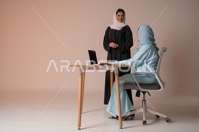  استخدام جهاز الحاسوب المحمول لمتابعة ومناقشة الأعمال، اداء المهام للتطور المهني وتحقيق الاهداف, الشراكة والتعاون في إنجاز المهام، بورتريه لسيدتان عربيتان خليجيتات سعوديتان محجبتان في اجتماع عمل، دراسة وتحليل المشاريع الجديدة، خلفية بيج