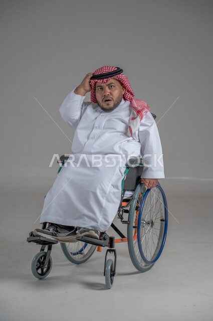 Lifestyle of people with disabilities, using a wheelchair to assist with mobility and transportation, portrait of a young Saudi Arabian Gulf dwarf with disabilities wearing traditional thobe and shemagh sitting on a wheelchair moving his hands with gestures of pleasure, full body image, gray background