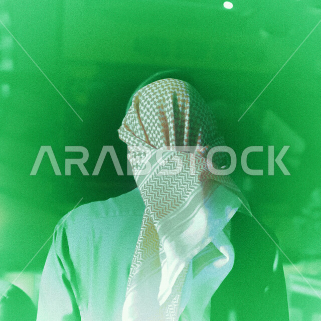 منظر من الخلف لرجل سعودي خليجي يقوم بجلسة تصوير بخلفية خضراء ، يرتدي زي تقليدي سعودي مع شماغ وعقال