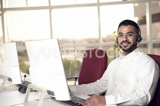 A Saudi Arabian Gulf employee working in customer service and wearing a headset, inquiries and inquiries, answering customer questions, making video calls through a computer, eyeglasses, follow-up and work development