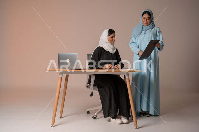 تبادل الأفكار والخبرات لتطوير استراتيجيات العمل، بورتريه لأمرأتان عربيتان سعوديتان خليجيتان محجبتان  يقومان بتطوير الخطط وحل المشكلات لتحقيق أهداف الشركة، الانتباه للملاحظات وتطبيقها، الجسم بالطول الكامل، خلفيه بيضاء