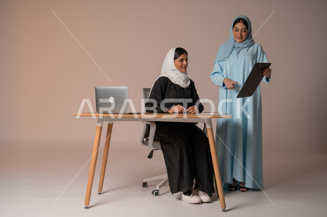 تبادل الأفكار والخبرات لتطوير استراتيجيات العمل، بورتريه لأمرأتان عربيتان سعوديتان خليجيتان محجبتان  يقومان بتطوير الخطط وحل المشكلات لتحقيق أهداف الشركة، الانتباه للملاحظات وتطبيقها، الجسم بالطول الكامل، خلفيه بيضاء