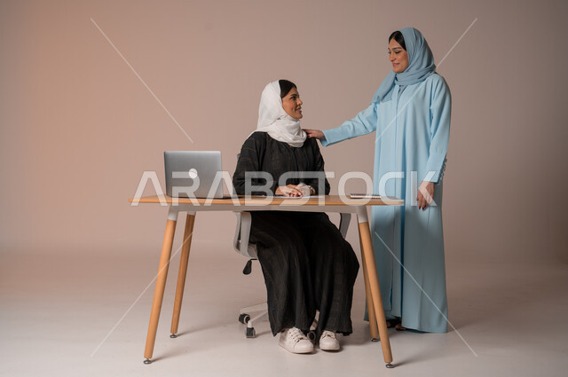 تدريب وتطوير الموظفين وتشجيعهم، الإجتماع في مقر العمل ومناقشة المهام، بورتريه لإمرأتان عربيتان خليجيتان سعوديتان محجبتان داخل مقر الشركة، بيئة عمل مريحة ومتطورة، العمل الجماعي وروح الفريق الواحد، الجسم بالطول الكامل، خلفية بيج