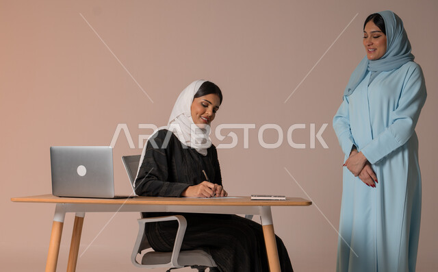 مراقبة حسن سير العمل، نمط الحياة وبيئة العمل السعودي، إمرأتان عربيتان خليجيتان سعوديتان محجبتان داخل مقر الشركة، العمل الجماعي وروح الفريق الواحد، ادارة الاعمال و المهام في غرفة الاجتماعات، خلفية بيج
