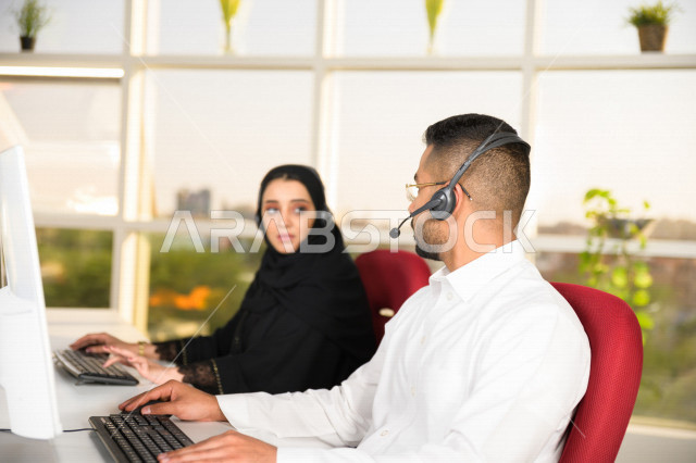 Two Saudi Arabian Gulf employees working in customer service, an employee and an employee wearing a headset, making inquiries and inquiries, answering customer questions, making video calls through a computer, following up and developing work