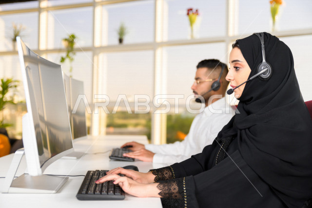 Two Saudi Arabian Gulf employees working in customer service, an employee and an employee wearing a headset, making inquiries and inquiries, answering customer questions, making video calls through a computer, following up and developing work