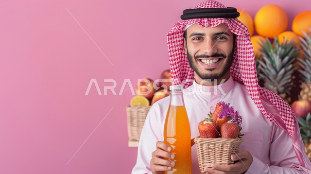 مفهوم الرجولة والاهتمام بالمظهر الخارجي، صورة مقربة لرجل عربي خليجي سعودي يرتدي الشماغ الاحمر والزي التقليدي يحمل بيده زجاجة عصير ونوع من الفواكه، النظر الى الكاميرا بتعابير السعادة والسرور، الاستمتاع بالمشروبات الباردة في الأجواء الحارة