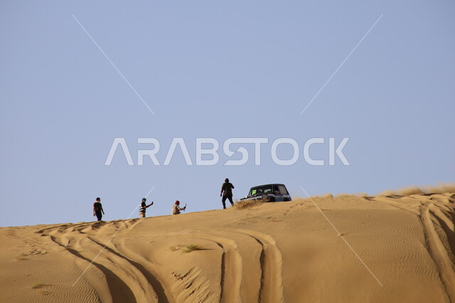 Driving vehicles in the Nawan desert in Al Baha region, enjoying practicing a favorite hobby (dune bashing), a group of men watching and photographing car racing in Saudi Arabia, doing recreational activities to attract tourists, going on adventures using a four-wheel drive vehicle in the deserts of the Kingdom