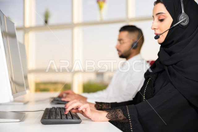 Two Saudi Arabian Gulf employees working in customer service, an employee and an employee wearing a headset, making inquiries and inquiries, answering customer questions, making video calls through a computer, following up and developing work
