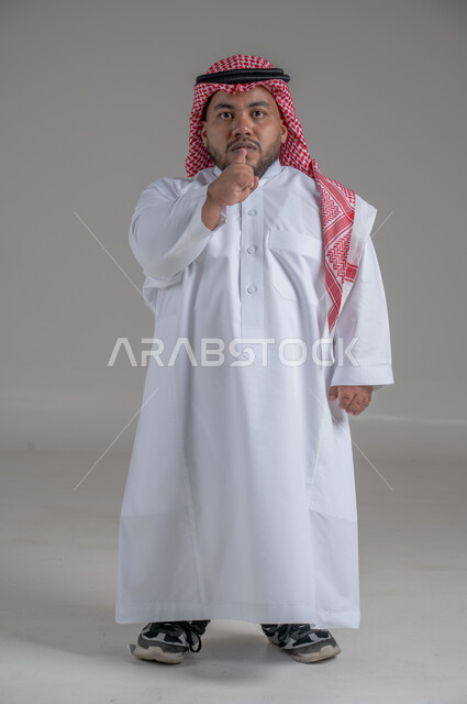 التمكين الاجتماعي لذوي الهمم، بورتريه لشاب عربي خليجي سعودي قصير القامة يرتدي الثوب التقليدي والشماغ يقوم بتحريك يديه بايماءات تدل على التوقف عن الكلام، صورة الجسم بالطول الكامل، خلفية رمادية