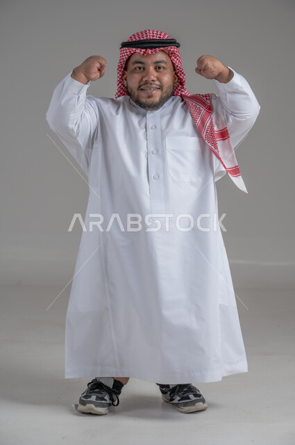 Social empowerment of people with disabilities, portrait of a short Saudi Arabian Gulf young man wearing traditional thobe and shemagh moving his hands in gestures indicating courage and strength, full body image, gray background
