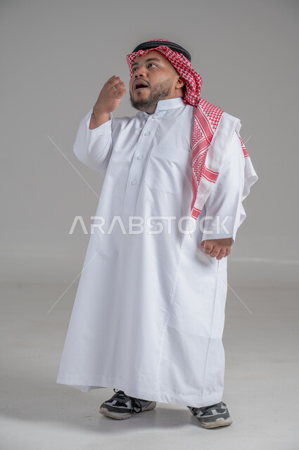 التمكين الاجتماعي لذوي الهمم، بورتريه لشاب عربي خليجي سعودي قصير القامة يرتدي الثوب التقليدي والشماغ يقوم بتحريك يديه بايماءات تدل على السعادة والسرور، صورة الجسم بالطول الكامل، خلفية رمادية