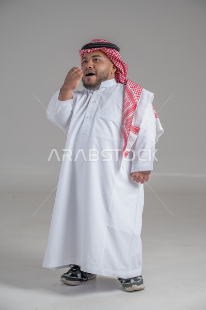 التمكين الاجتماعي لذوي الهمم، بورتريه لشاب عربي خليجي سعودي قصير القامة يرتدي الثوب التقليدي والشماغ يقوم بتحريك يديه بايماءات تدل على السعادة والسرور، صورة الجسم بالطول الكامل، خلفية رمادية