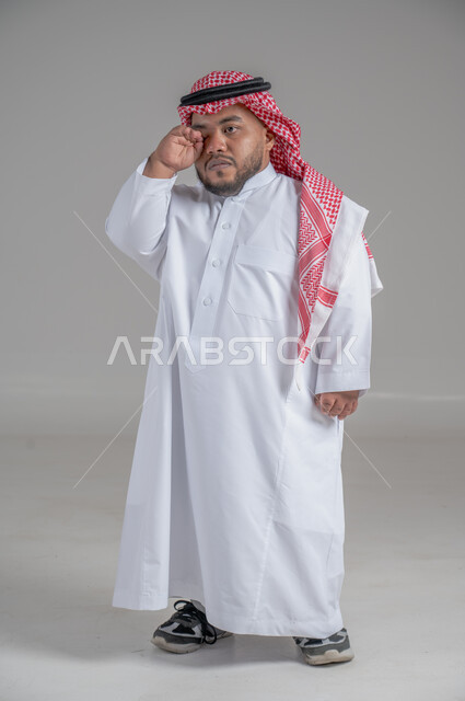 التمكين الاجتماعي لذوي الهمم، بورتريه لشاب عربي خليجي سعودي قصير القامة يرتدي الثوب التقليدي والشماغ يقوم بتحريك يديه بايماءات تدل على السعادة والسرور، صورة الجسم بالطول الكامل، خلفية رمادية