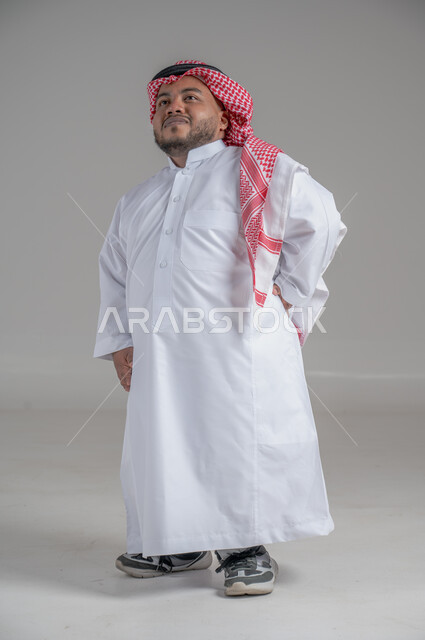 التمكين الاجتماعي لذوي الهمم، بورتريه لشاب عربي خليجي سعودي قصير القامة يرتدي الثوب التقليدي والشماغ يقوم بتحريك يديه بايماءات تدل على السعادة والسرور، صورة الجسم بالطول الكامل، خلفية رمادية