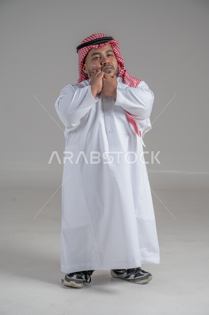التمكين الاجتماعي لذوي الهمم، بورتريه لشاب عربي خليجي سعودي قصير القامة يرتدي الثوب التقليدي والشماغ يقوم بتحريك يديه بايماءات تدل على السعادة والسرور، صورة الجسم بالطول الكامل، خلفية رمادية