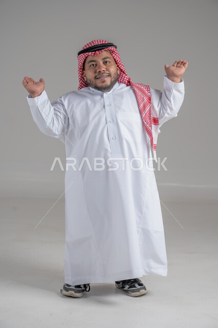 التمكين الاجتماعي لذوي الهمم، بورتريه لشاب عربي خليجي سعودي قصير القامة يرتدي الثوب التقليدي والشماغ يقوم بتحريك يديه بايماءات تدل على السعادة والسرور، صورة الجسم بالطول الكامل، خلفية رمادية