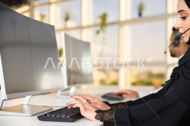 Two Saudi Arabian Gulf employees working in customer service, an employee and an employee wearing a headset, making inquiries and inquiries, answering customer questions, making video calls through a computer, following up and developing work