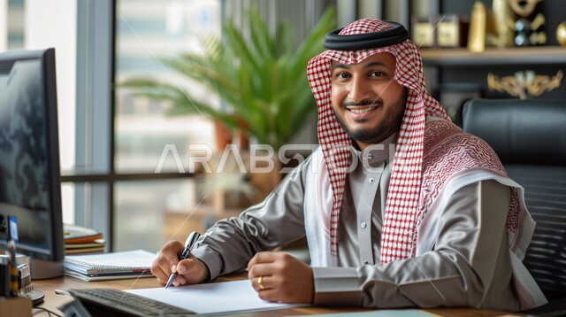 Comfortable work environment in Saudi companies, close-up of a Saudi Arabian Gulf businessman wearing traditional thobe and shemagh sitting inside the office at the company headquarters taking notes, looking at the camera with expressions of joy and happiness, office administrative jobs and professions