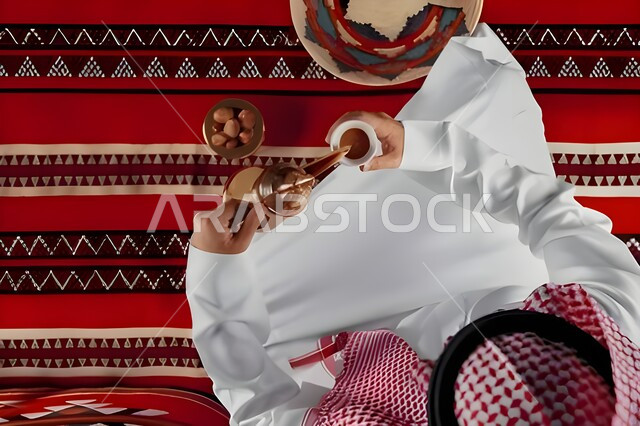 Enjoying hot drinks, following Saudi customs and traditions in serving Arabic coffee in a copper pot and cup, good hospitality and reception among Arabs, local national products, vertical top view of a Halaj Arab man wearing a traditional thobe and shemagh pouring coffee