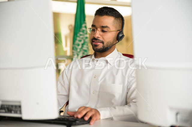 A Saudi Arabian Gulf employee working in customer service and wearing a headset, inquiries and inquiries, answering customer questions, making video calls through a computer, eyeglasses, follow-up and work development