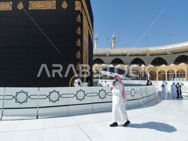 وضع الحرم المكي الشريف في أيام انتشار فايروس كورونا في المملكة العربية السعودية ، رجل عربي خليجي سعودي يرتدي الكمامة يطوف حول الكعبه، اتباع اجراءات الوقاية و السلامة من كوفيد ١٩، اداء مناسك العمره في مكة المكرمة ، معالم اسلاميه دينية مشهورة في السعودية