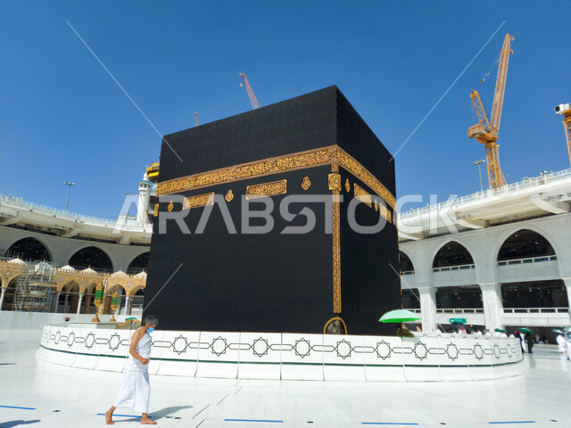 وضع الحرم المكي الشريف في أيام انتشار فايروس كورونا في المملكة العربية السعودية ، رجل عربي خليجي سعودي يرتدي الكمامة يطوف حول الكعبه، اتباع اجراءات الوقاية و السلامة من كوفيد ١٩، اداء مناسك العمره في مكة المكرمة ، معالم اسلاميه دينية مشهورة في السعودية