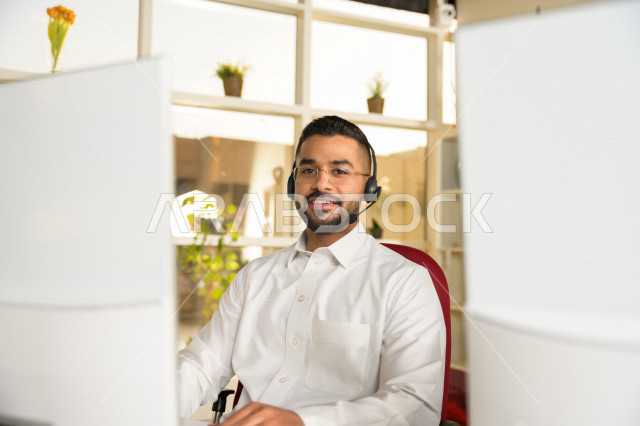 A Saudi Arabian Gulf employee working in customer service and wearing a headset, inquiries and inquiries, answering customer questions, making video calls through a computer, eyeglasses, follow-up and work development