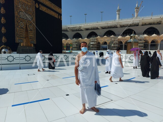 أماكن العبادة والتقرب الى الله, أداء المسلمون لمناسك العمرة وقت إجراءات الحظر الصحي تفاديا لإنتشار فيروس كورونا كوفيد 19 ، الإجراءات الواقائية في المكة المكرمة، صورة مقربة لرجل مسلم خليجي عربي سعودي يرتدي الكمامة الواقية و ملابس الاحرام ينظر الى الكاميرا، صورة الجسم بالطول الكامل