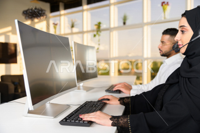 Two Saudi Arabian Gulf employees working in customer service, an employee and an employee wearing a headset, making inquiries and inquiries, answering customer questions, making video calls through a computer, following up and developing work