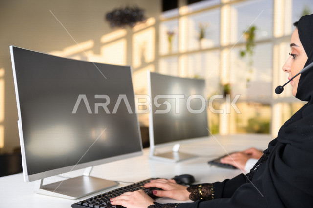 Two Saudi Arabian Gulf employees working in customer service, an employee and an employee wearing a headset, making inquiries and inquiries, answering customer questions, making video calls through a computer, following up and developing work