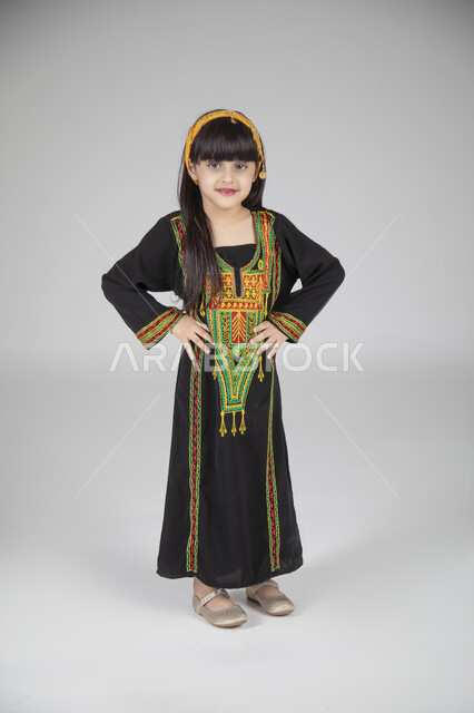 الاحتفال بيوم التأسيس والمناسبات الوطنية الشعبية، بورتريه لبنت عربية خليجية سعودية ترتدي الزي المطرز التقليدي السعودي النسائي تقف وتنظر إلى الكاميرا بإيماءات العز والفخر، ارتداء الأزياء التراثية القديمة، الجسم بالطول الكامل، خلفية رمادية