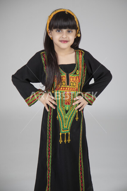 الاحتفال بيوم التأسيس والمناسبات الوطنية الشعبية، بورتريه مقرب لبنت عربية خليجية سعودية ترتدي الزي المطرز التقليدي السعودي النسائي تقف وتنظر إلى الكاميرا بإيماءات السعادة، مشاعر العز والفخر بالانتماء الوطني، ارتداء الأزياء التراثية القديمة، خلفية رمادية